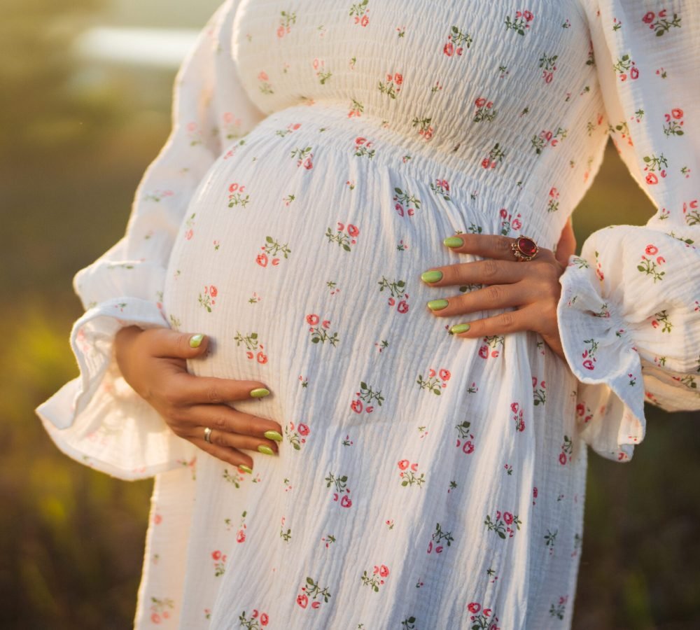 Happy Mother Carrying Child, Expecting For Baby. Amazing Motherhood. Pregnant Woman in beautiful dress on nature backdrop, rural meadow. High quality